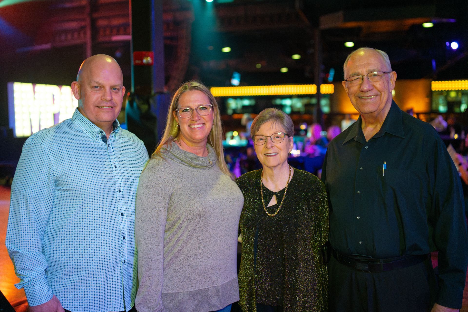 Four people smiling at a party; two men and two women. Indoors, with a bar in the background.