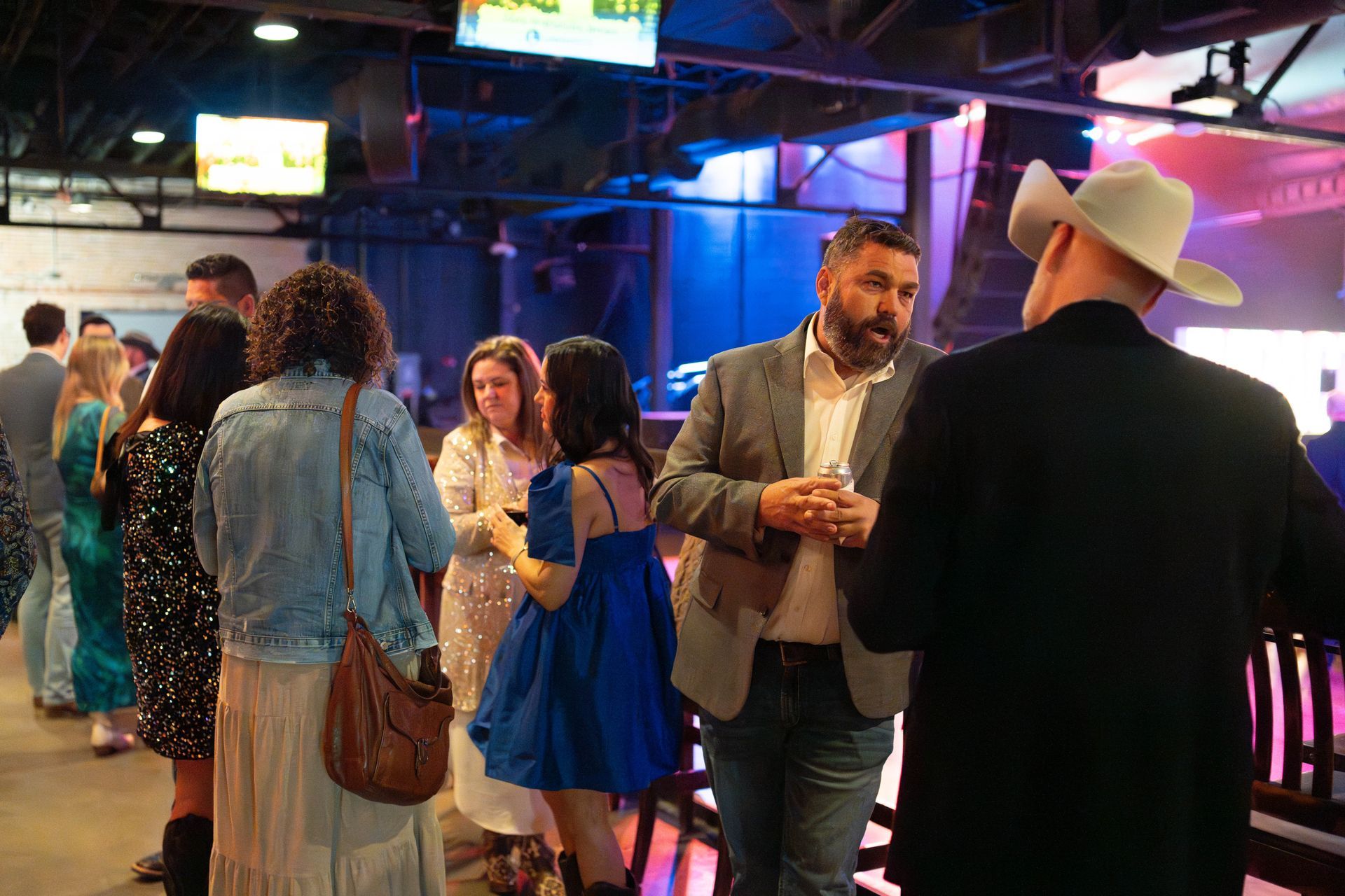 People socializing at an event; a man in a cowboy hat and another in a suit converse.