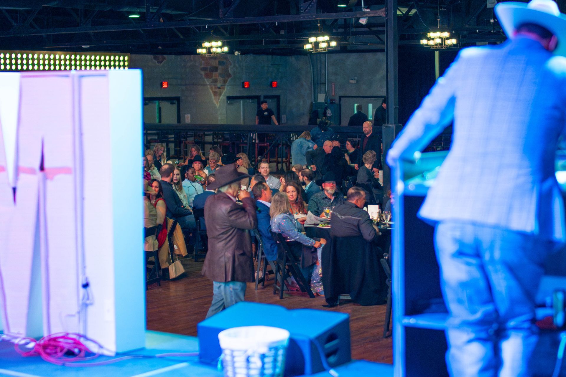 Event with a singer on stage; audience in a large room, some wearing cowboy hats.