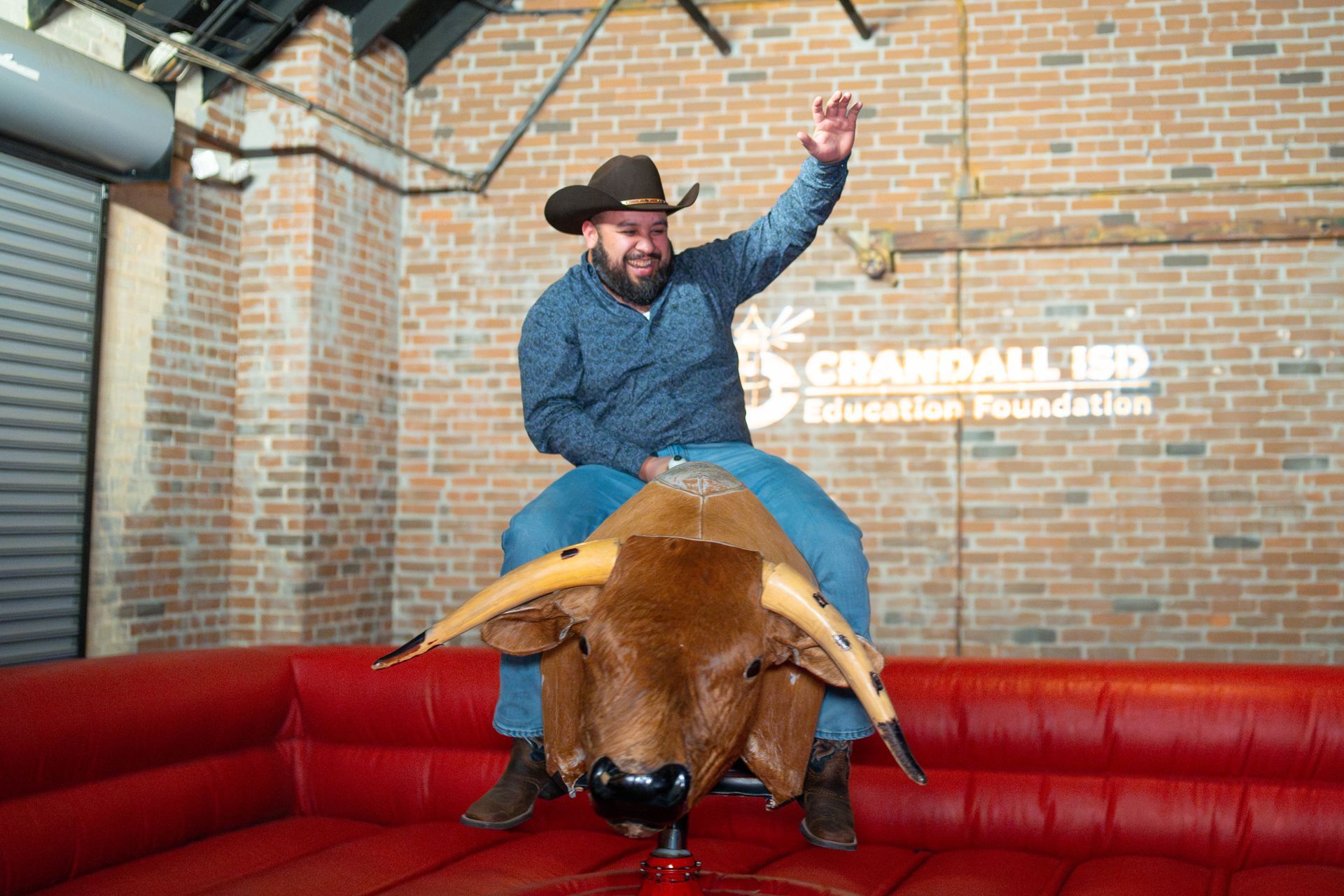 Man riding a mechanical bull, waving, at the Grandhall Education Foundation event.