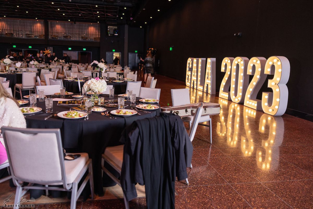 Large ballroom set for a gala. Black tablecloths, round tables, and illuminated 