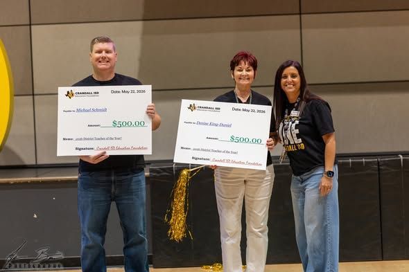 Three people on stage holding large check presentations, smiling at a recognition event.