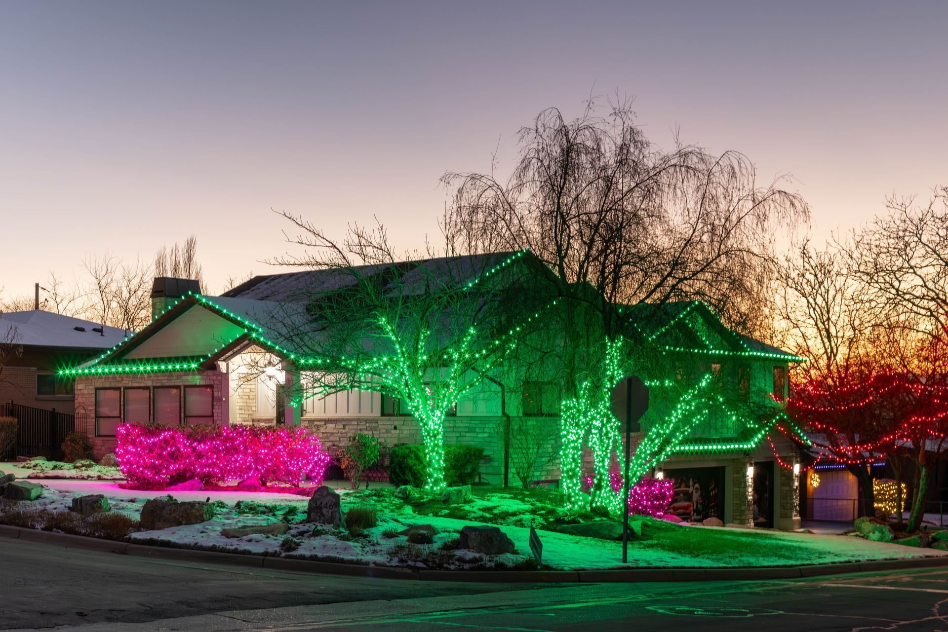 House and yard lit with green and pink holiday lights at dusk