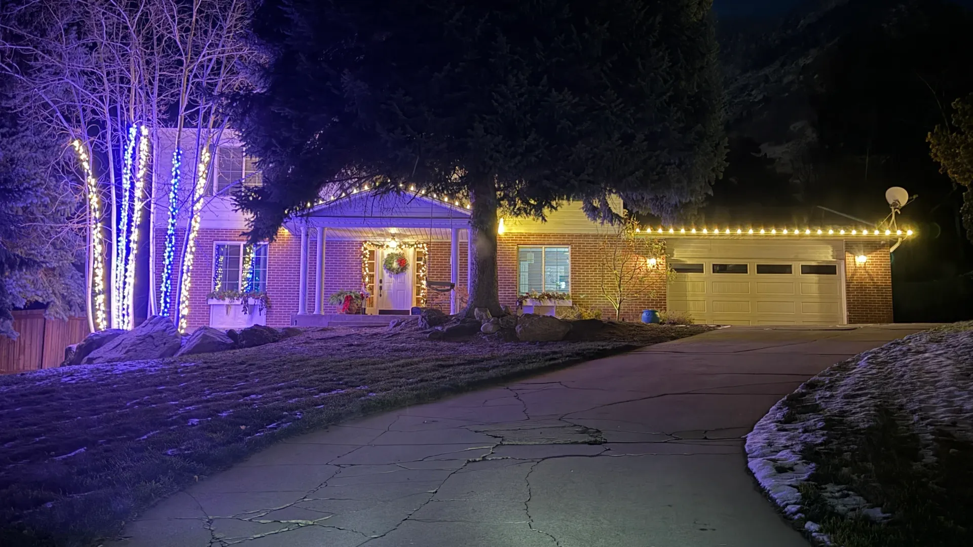 Snowy suburban house decorated with purple and warm white holiday lights at night