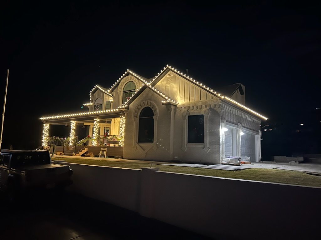 House at night outlined with warm white holiday lights, viewed from the street.