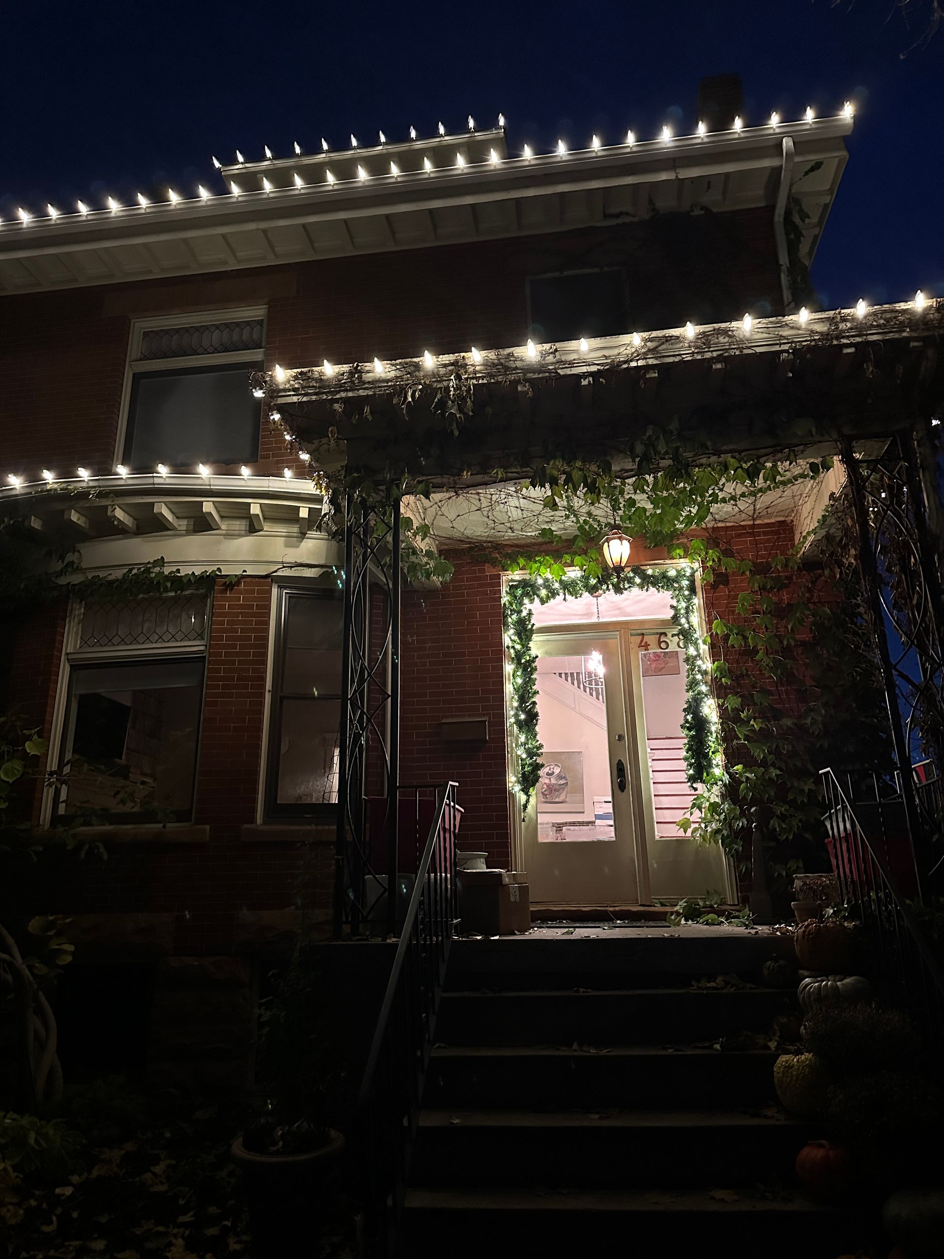 Red brick house at night, decorated with white Christmas lights on the roof and doorway.