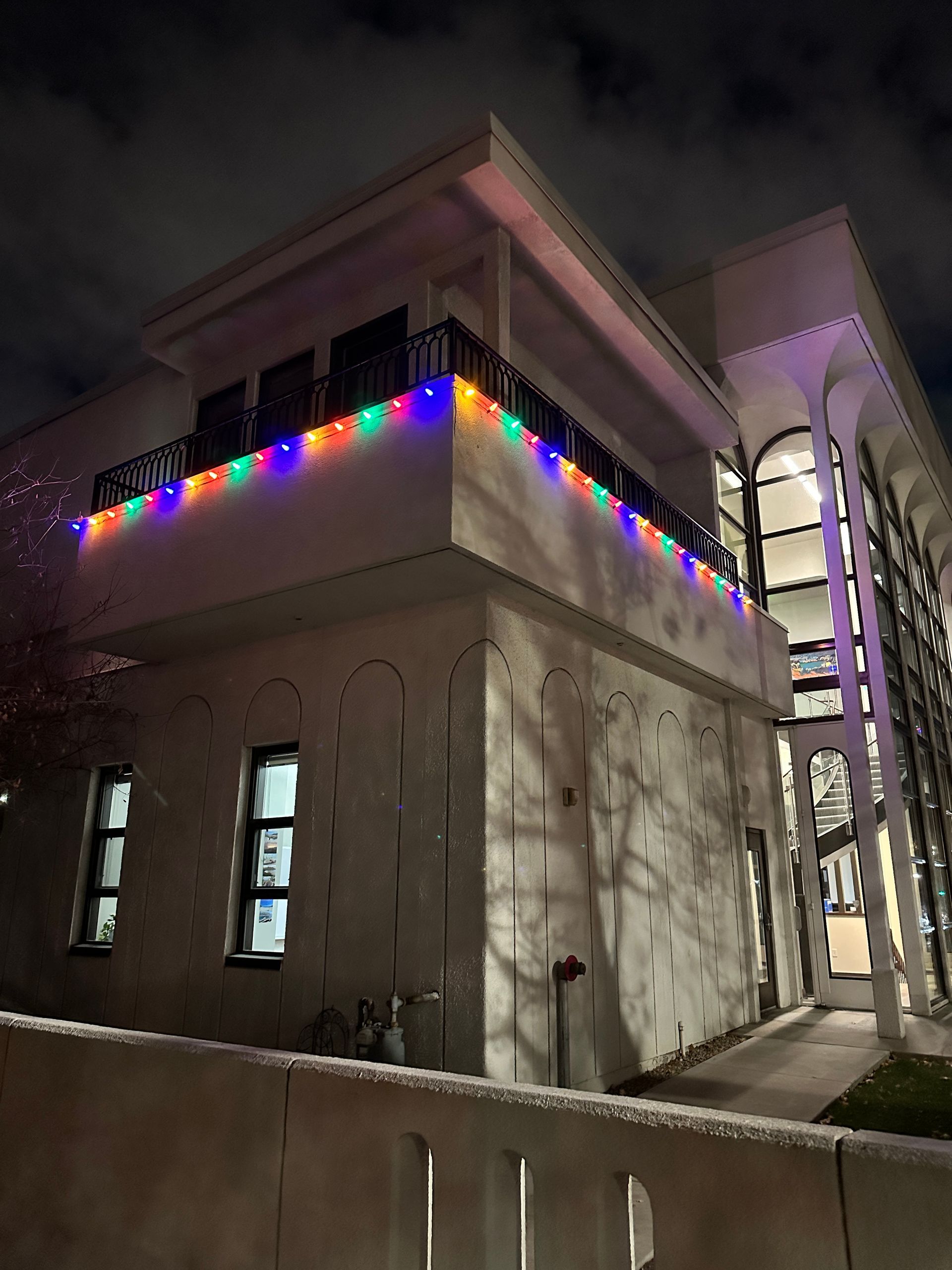 Building exterior at night with colorful string lights, white walls, and arched design.