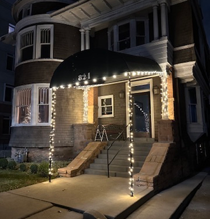 A brick building entrance at night, lit with string lights on the awning and pillars. The address is 821.