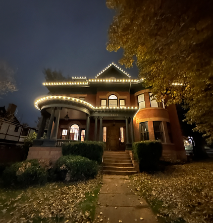 A large brick house at night, lit with white lights along the roofline.