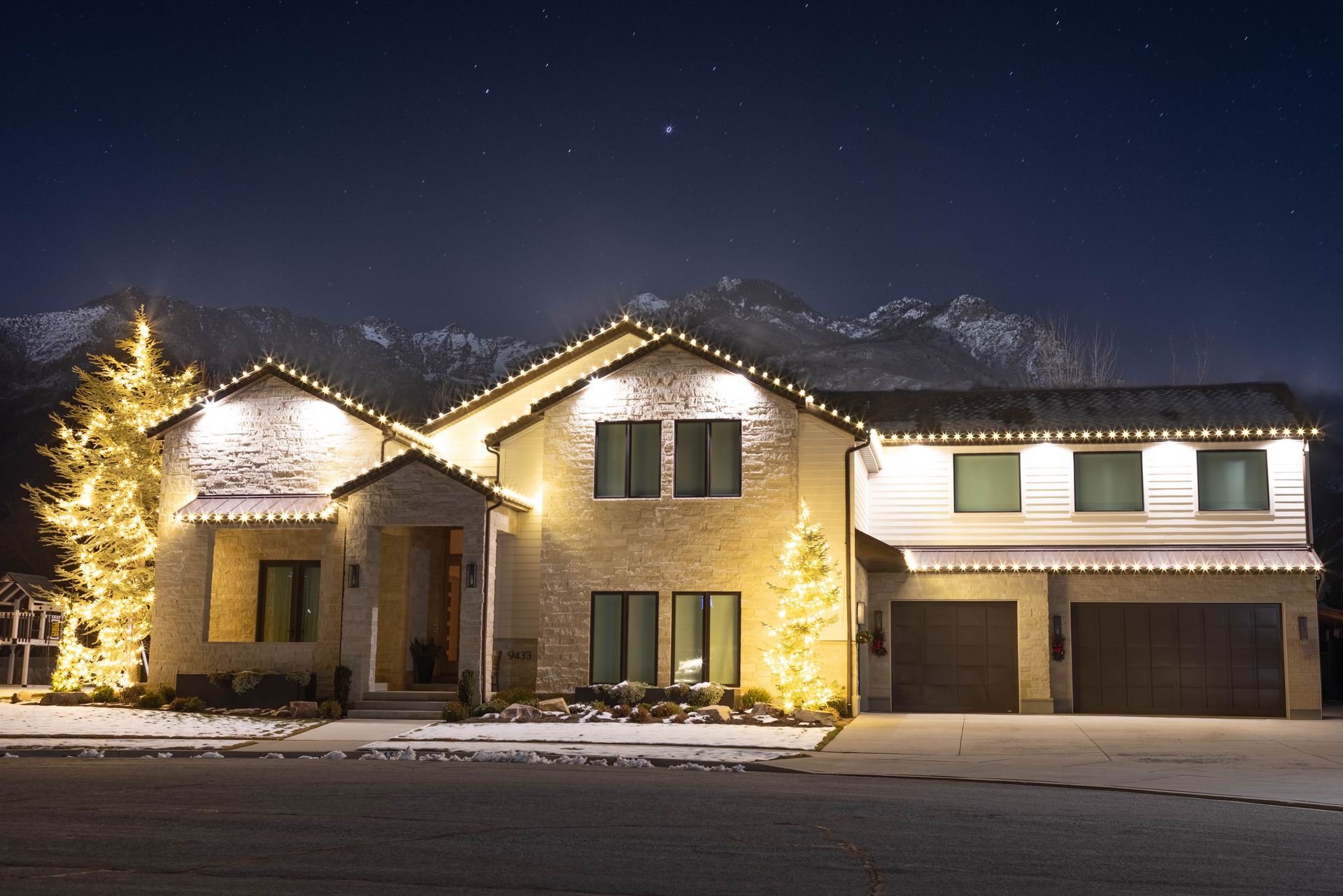 Snow-covered suburban house lit with holiday lights at night