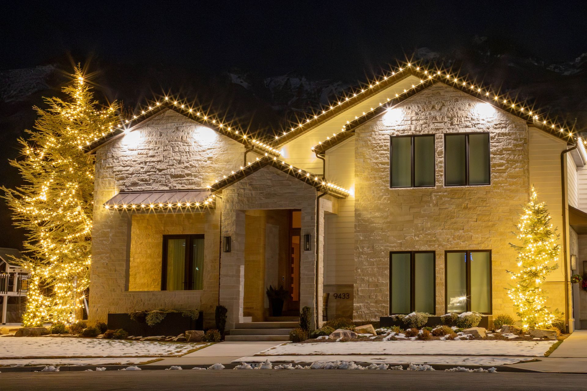 Snowy house decorated with warm white Christmas lights at night