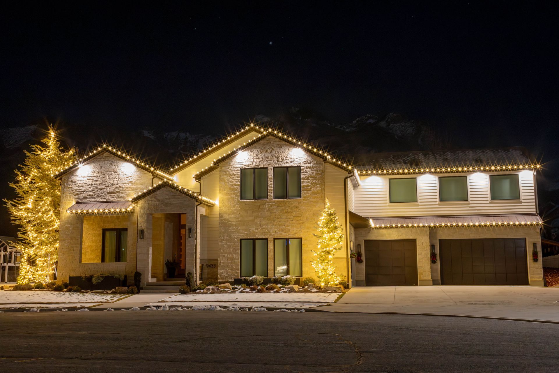 Snow-dusted suburban house at night outlined with warm white holiday lights