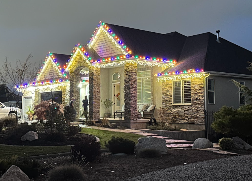 House with colorful Christmas lights illuminating the roof and facade at dusk.