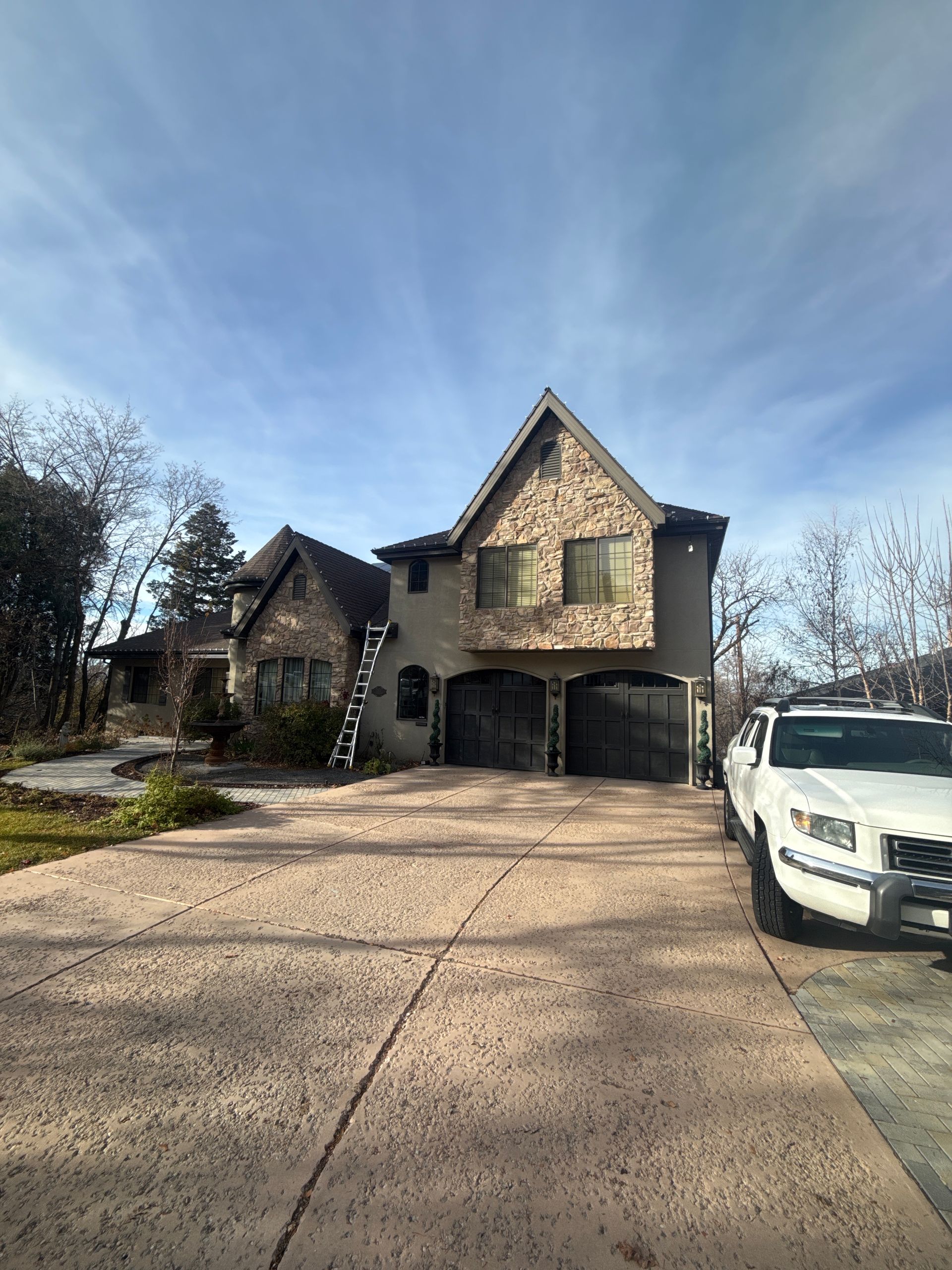 Stone house with arched garage doors and a white SUV parked in the driveway under a blue sky