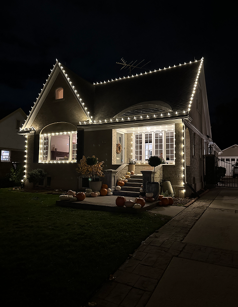 House decorated with white lights and pumpkins for the holiday season.