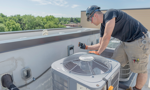 Technician inspecting an HVAC unit on a rooftop, with tools and nearby equipment.