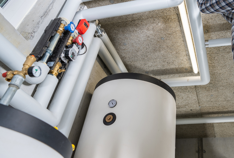 Industrial pipes and valves above a white tank in a utility room.