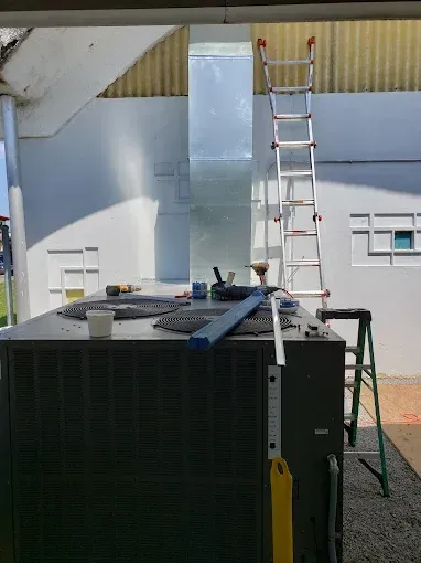 Rooftop HVAC unit beside a ladder and rooftop vent in an industrial courtyard