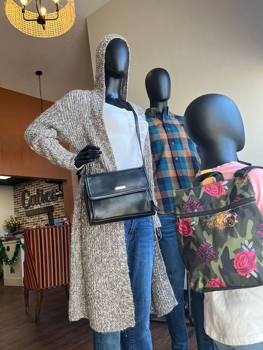 Three mannequins in a clothing store, styled in patterned coats, jeans, and a floral top with black bag