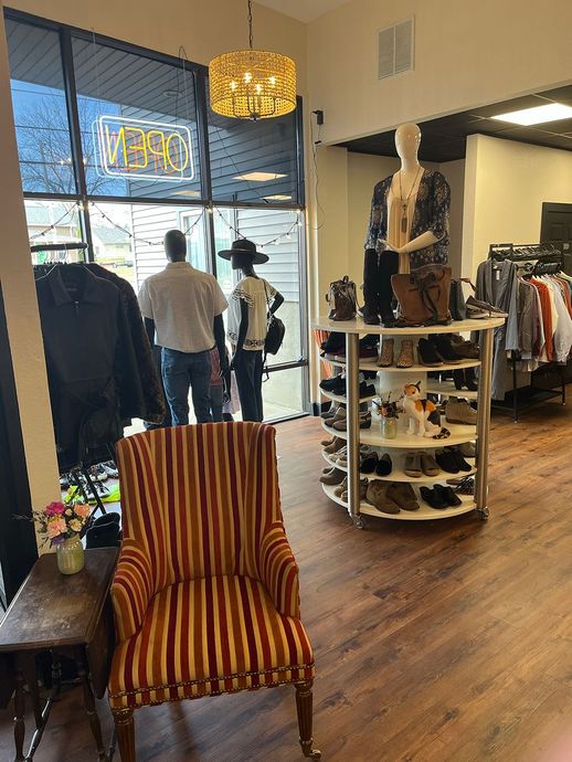Clothing store interior with striped chair, racks of clothes, and a neon sale sign by the window