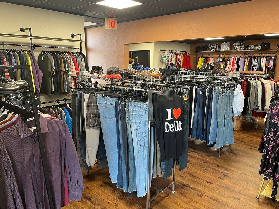 Clothing store interior with racks of jeans, shirts, and jackets on a wood floor.