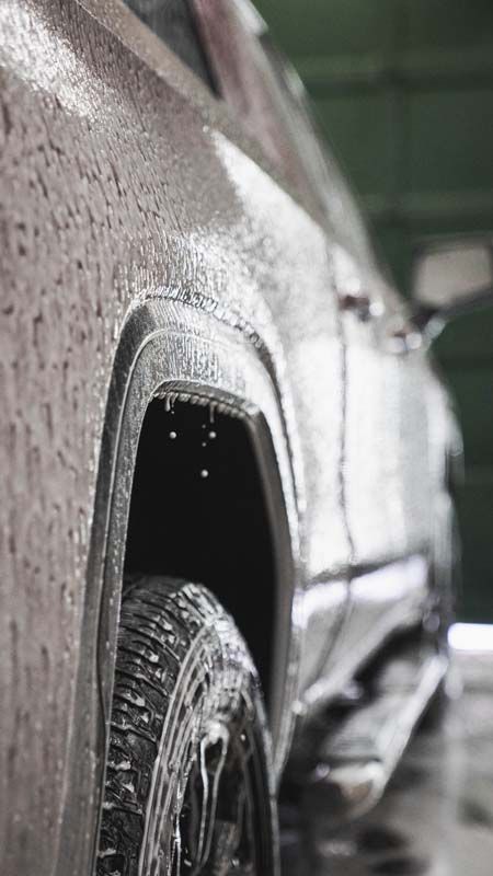 Truck being washed, covered in soapy water, in a car wash bay.