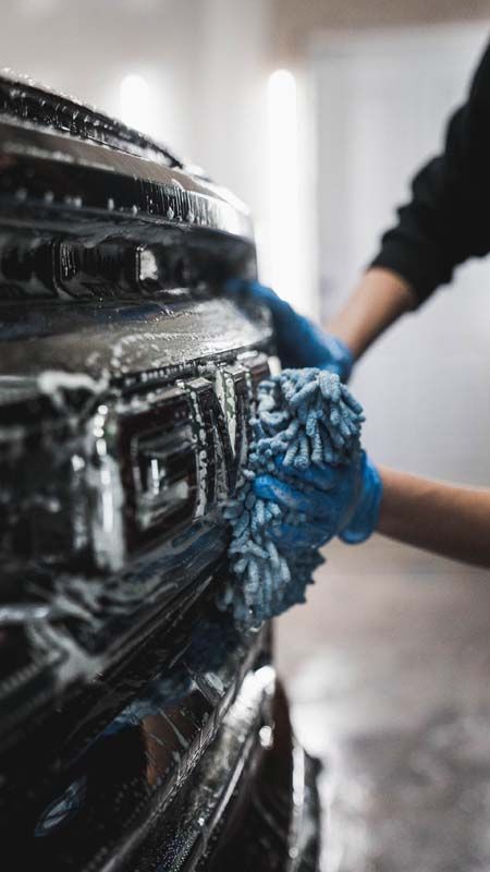Hands in blue gloves washing a black truck grille with a blue microfiber cloth.