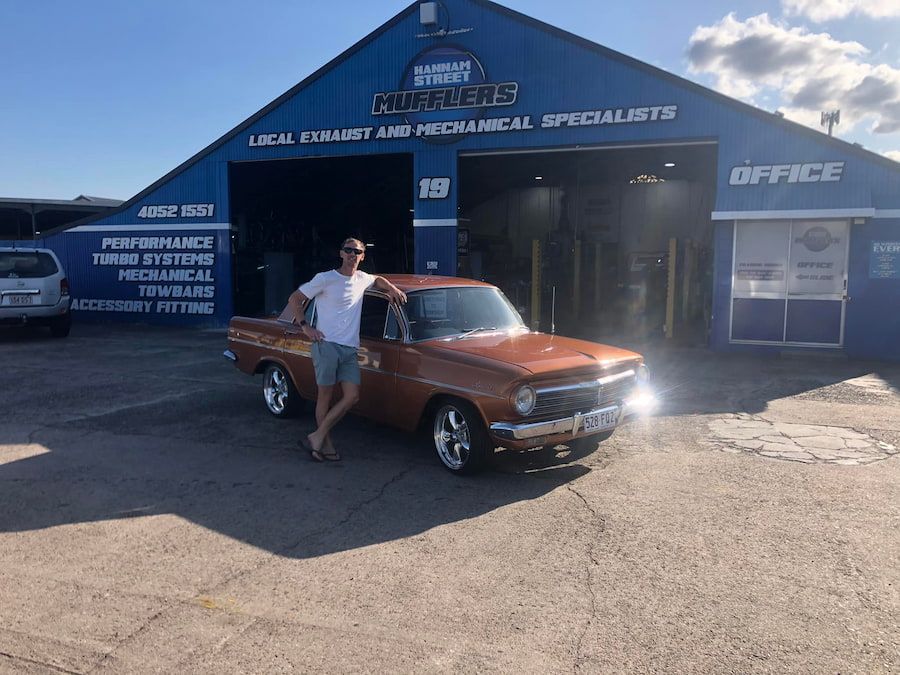 A Man Is Standing Next To A Car In Front Of A Building — Hannam Street Mufflers and Mechanical In Bungalow, QLD