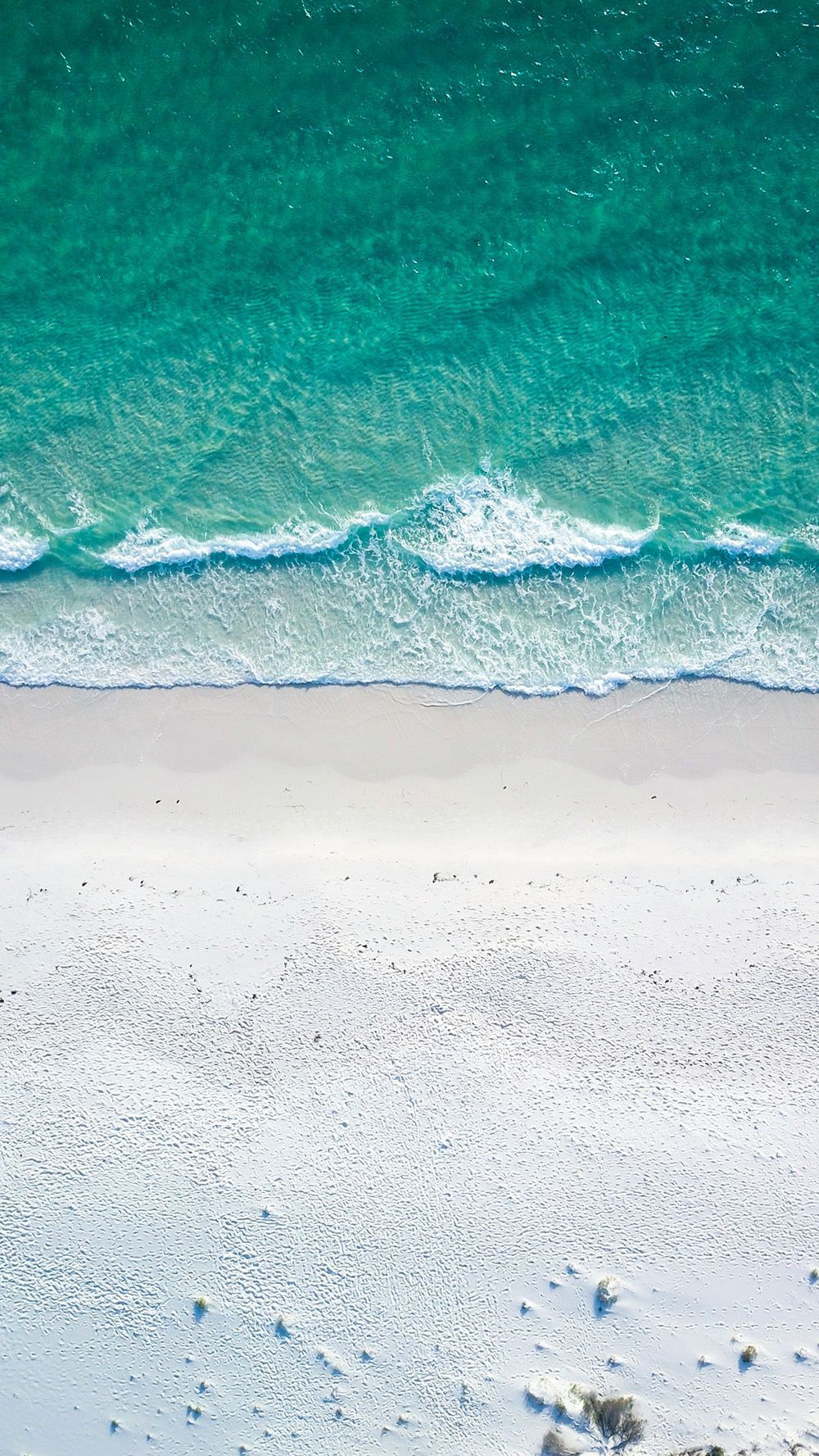 Aerial view of turquoise waves washing onto a white sandy beach.
