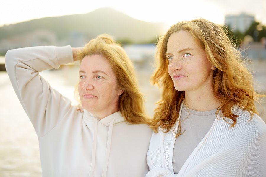 Two women standing outdoors in soft sunlight, one shielding her eyes and both looking into the distance.