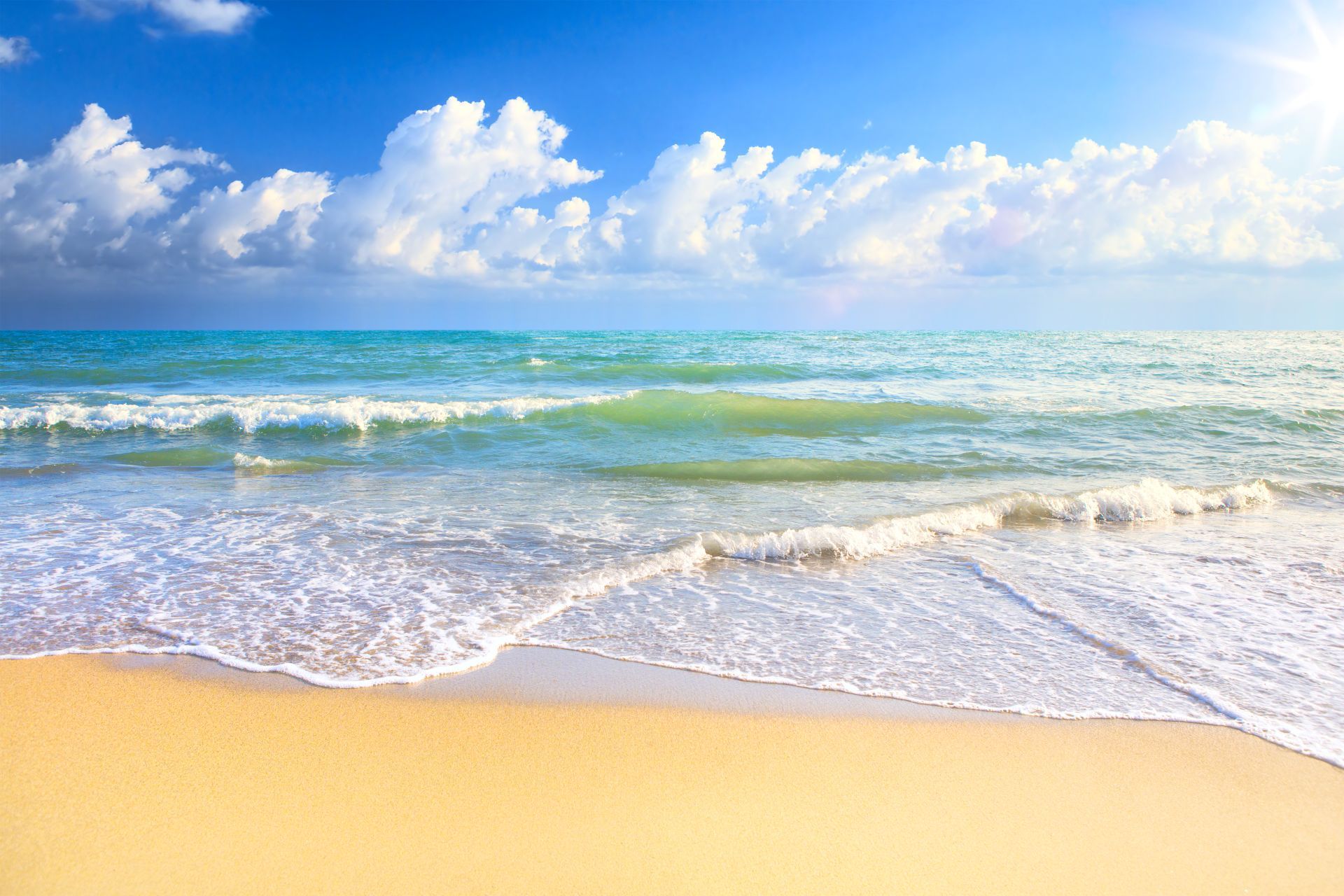 Sunny beach with gentle waves, golden sand, and a bright blue sky with fluffy clouds