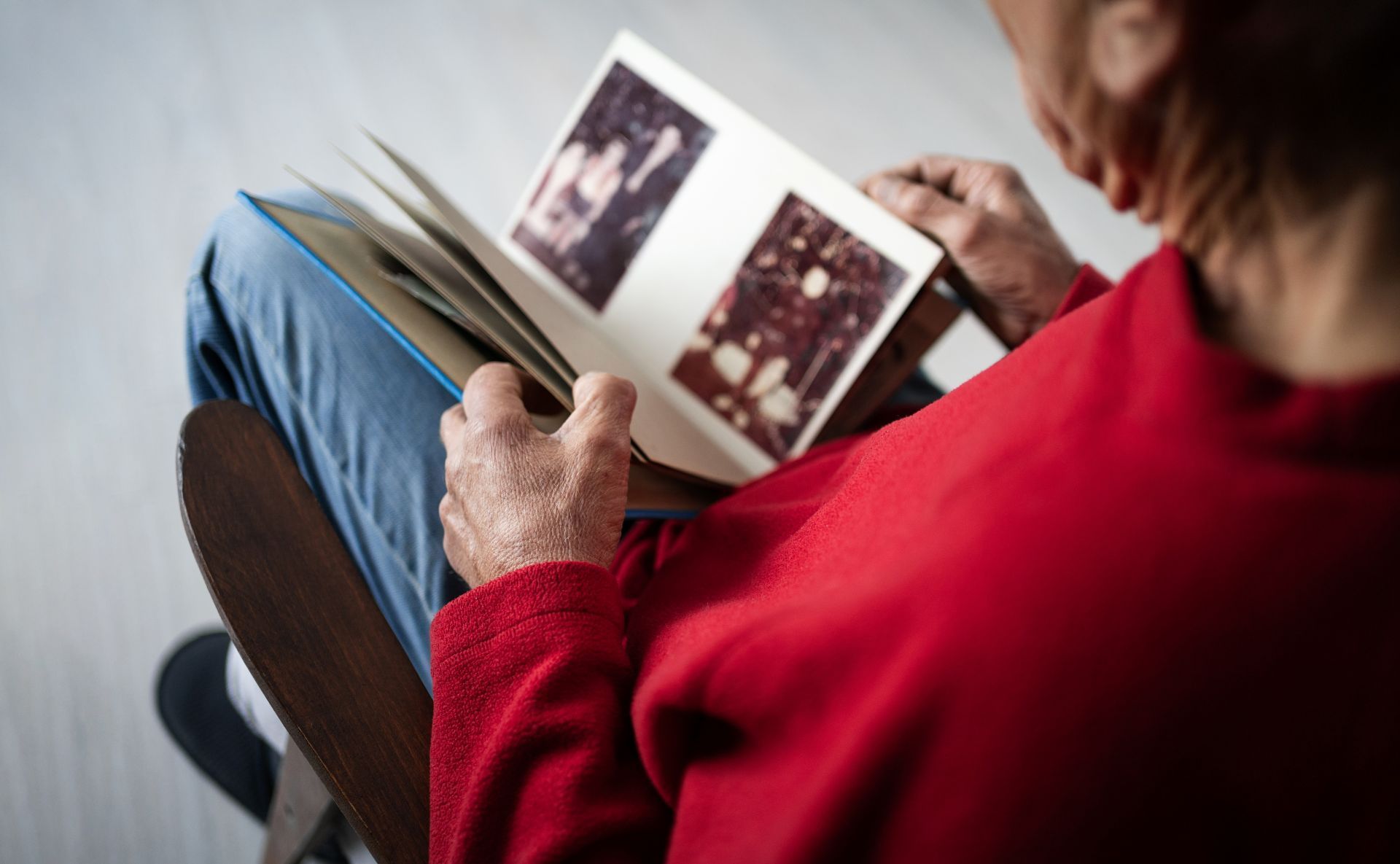 Person in red sweater looking through a photo album while seated on a couch