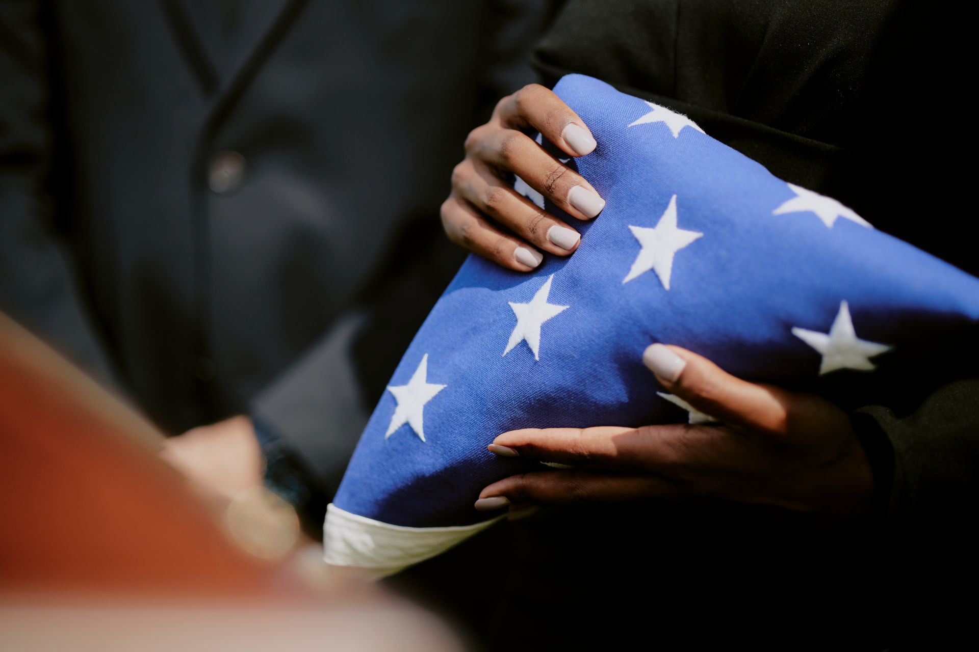 Hands holding a folded American flag with white stars on a blue field