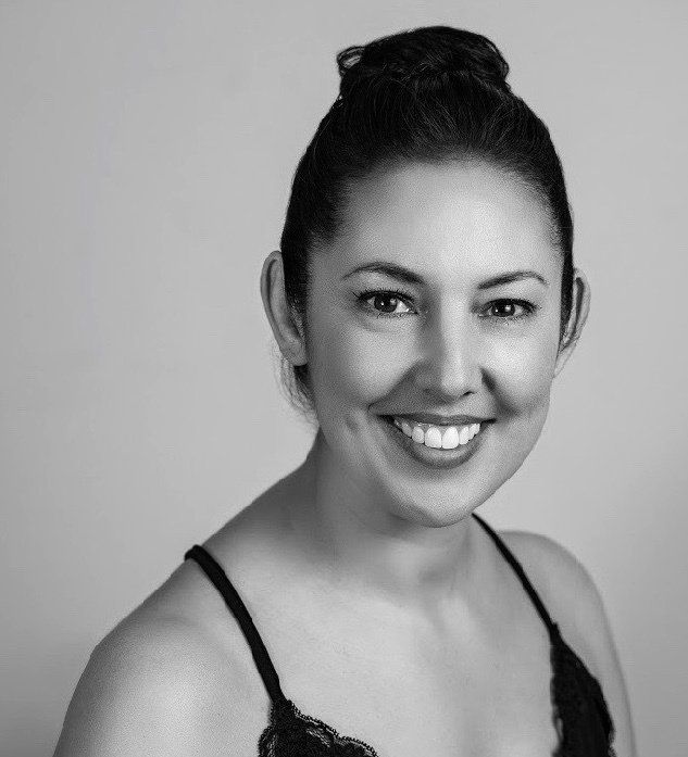 A woman in a black bra is smiling in a black and white photo.