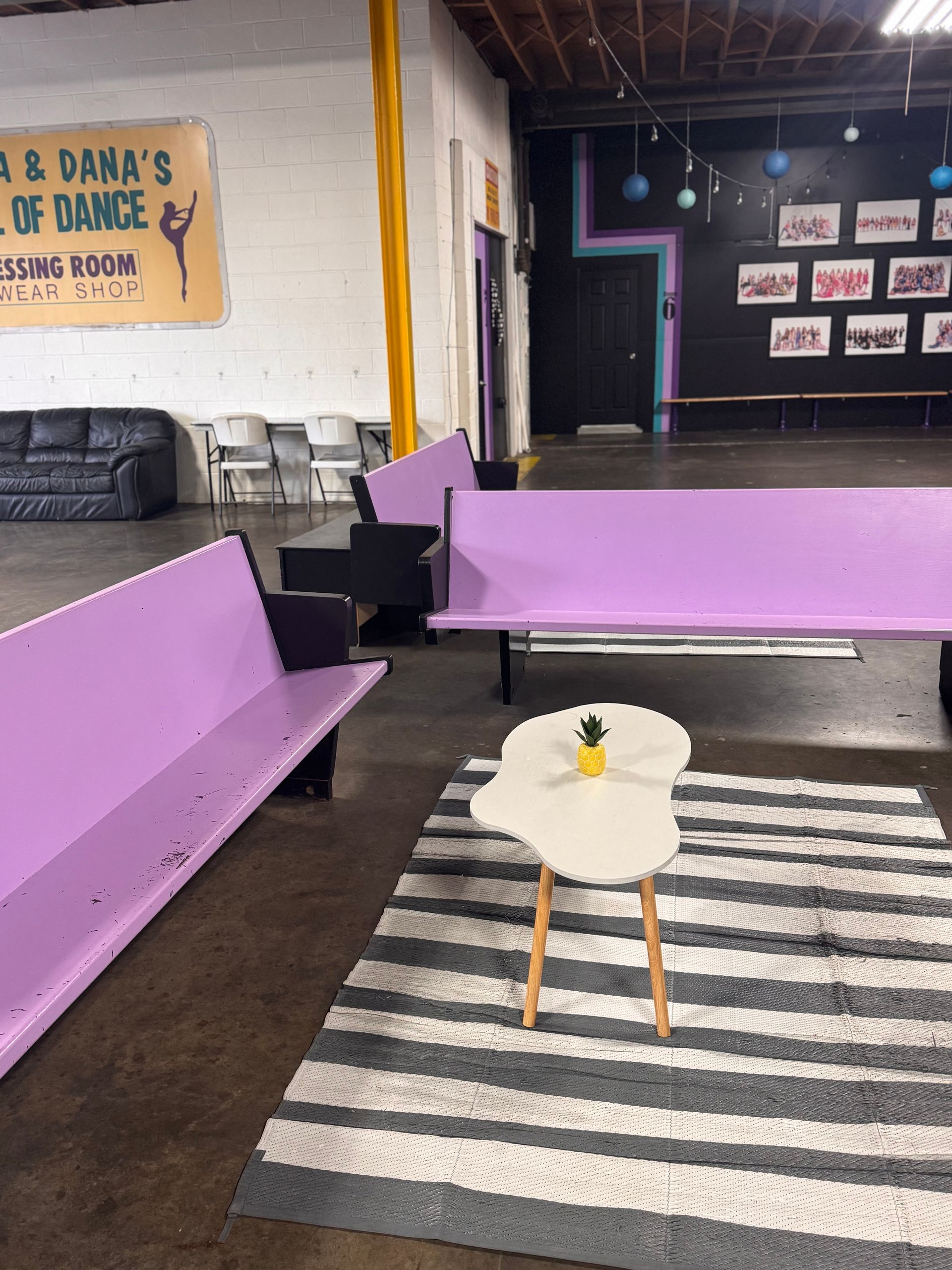A waiting area with two purple benches, a small white coffee table with a tiny pineapple on it, and a striped rug.