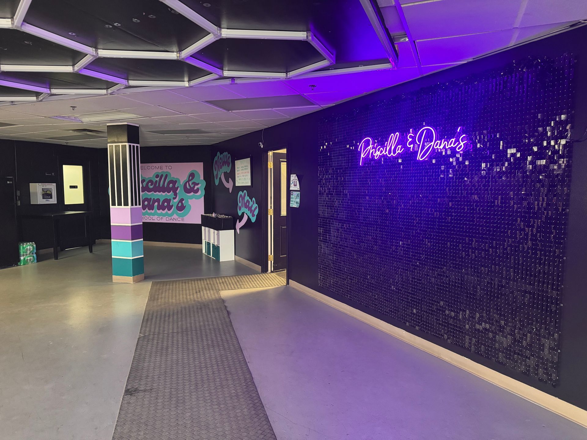 An interior shot of a modern lounge with purple lighting, a geometric ceiling, and a sparkling wall with neon text.