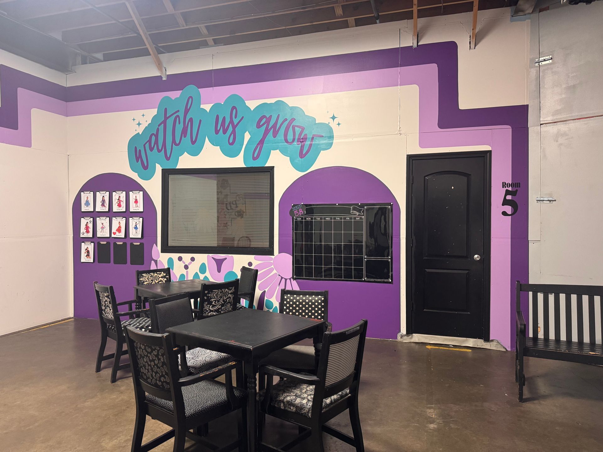 A waiting area featuring a table, chairs, a blackboard, and a purple-painted wall with the phrase