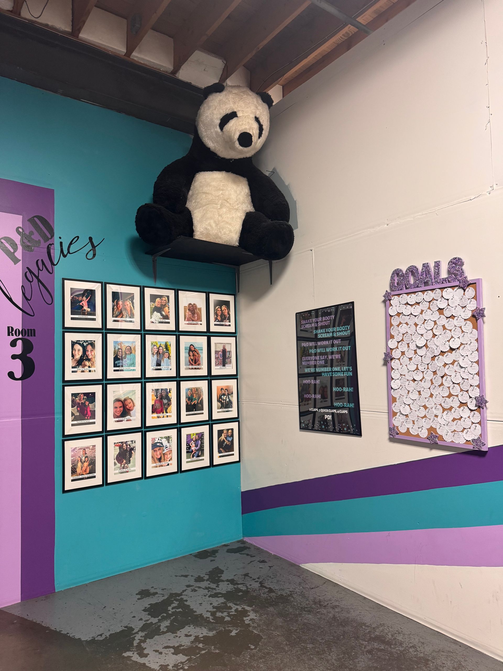 A teal wall features a large stuffed panda, a grid of framed photos, a chalkboard menu, and a bulletin board of notes.