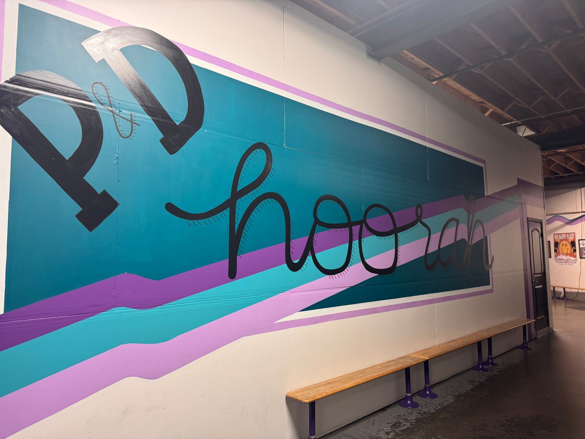 A teal wall with purple and lavender stripes features the black text
