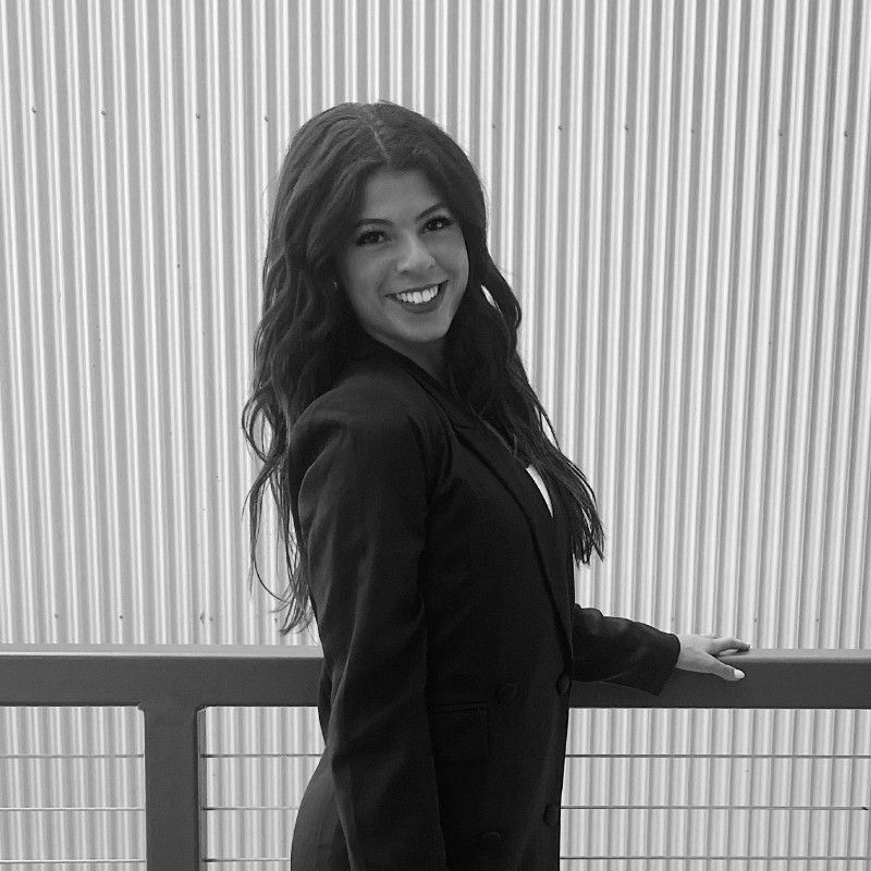 A black and white photo of a woman in a suit standing next to a railing.