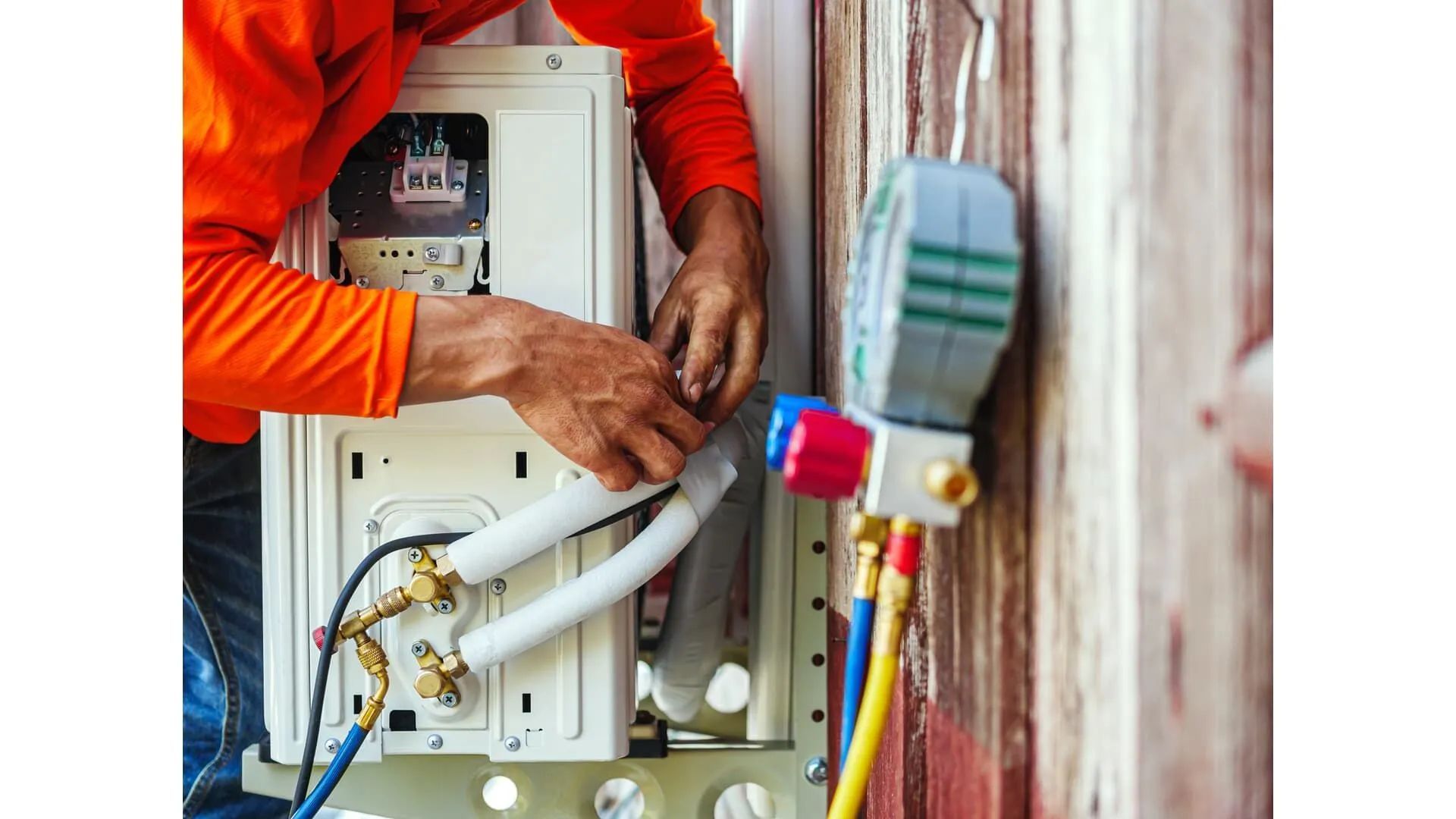 Technician in orange shirt working on electrical wiring inside an open utility box