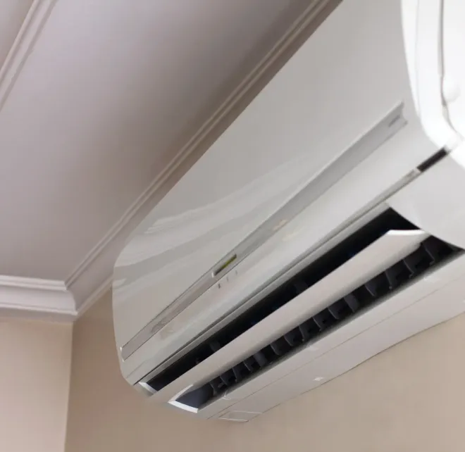 A white outdoor air conditioning unit mounted on a brown brick wall next to a window.