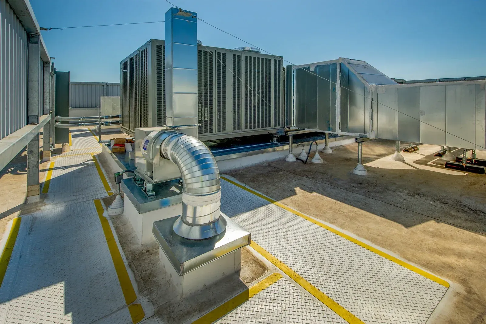 Industrial HVAC equipment on a gravel-covered rooftop with yellow safety lines under a clear blue sky.