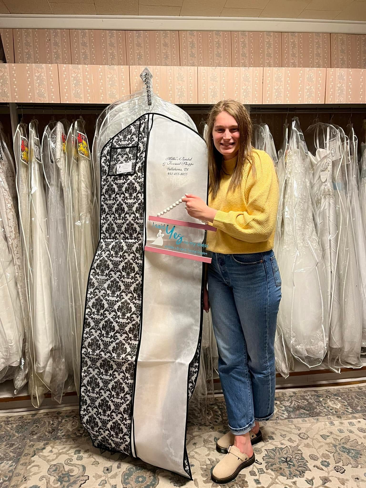 Woman in a yellow sweater holding a floral-and-white garment bag in a clothing showroom