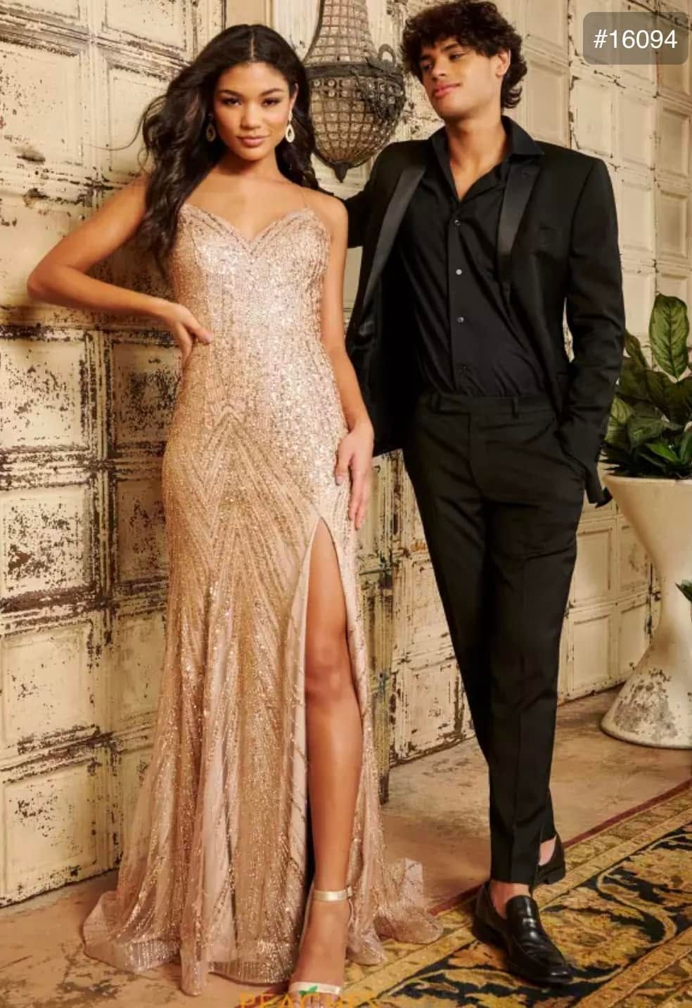 Two people posing in formal outfits against a stone wall, one in a shimmering gown and one in a black suit.