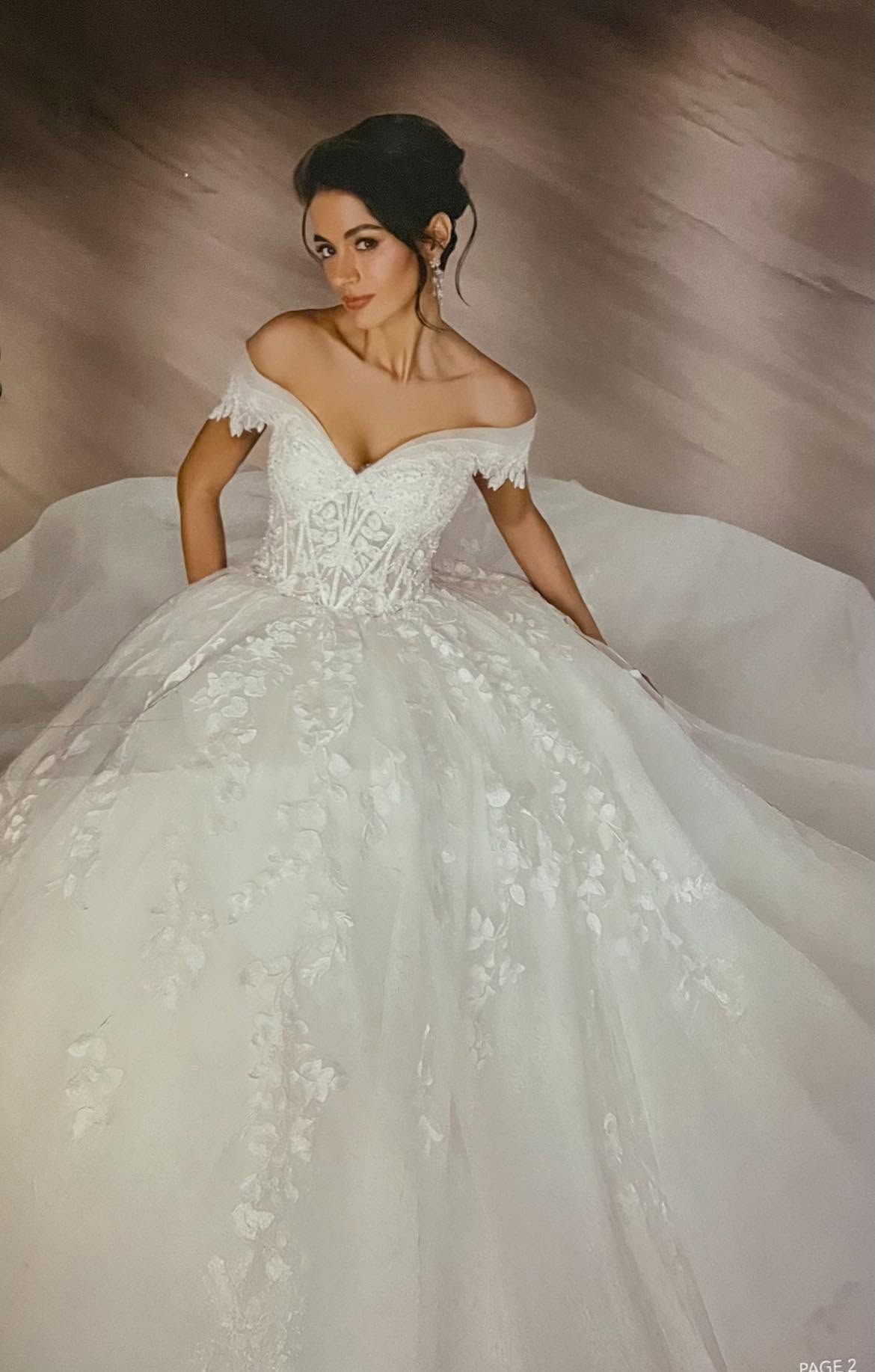 Woman in a white off-the-shoulder ball gown with a full tulle skirt, posing against a soft brown backdrop