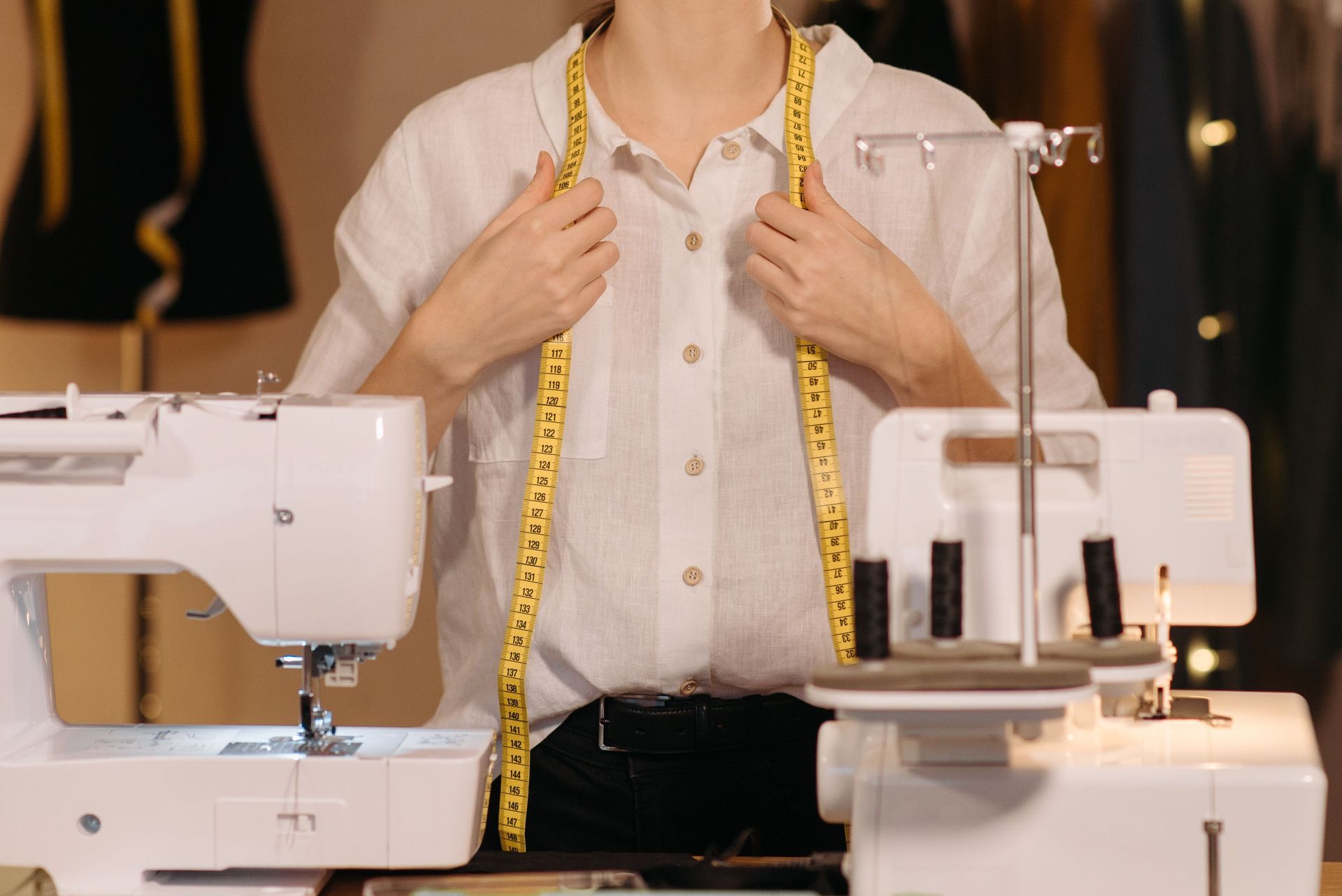 Person measuring their chest with a tape measure between two sewing machines