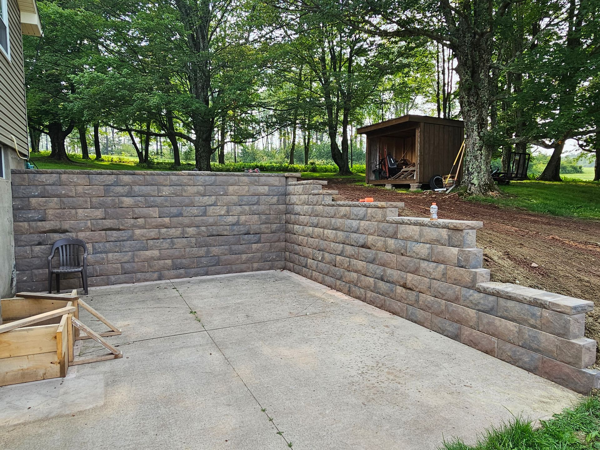 Concrete patio with stone retaining walls and a wooded backyard