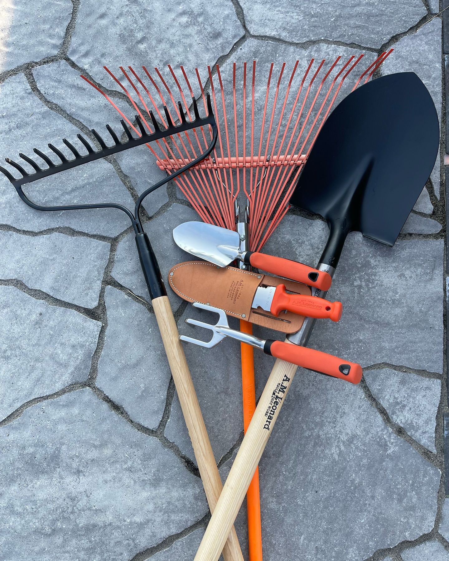 Garden tools—rakes, shovel, trowel, and hoe—lying on a cracked stone surface.