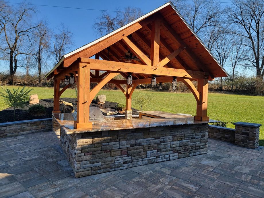 Wooden pavilion with a stone base in a landscaped park on a sunny day